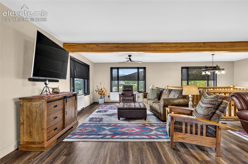 Image 11 of 45: Spacious living area featuring wood-finish flooring, exposed ceiling beams,