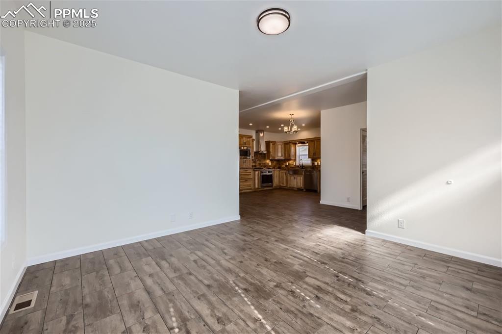 Image 4 of 16: Unfurnished living room with a chandelier and dark wood-style flooring