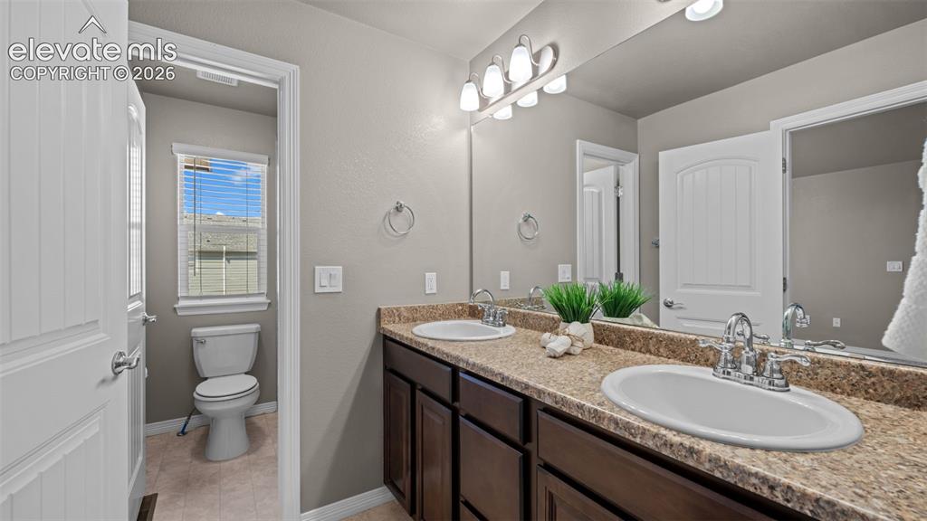Image 24 of 43: Dual vanity with undermount sinks, speckled countertop, and dark wood-finis