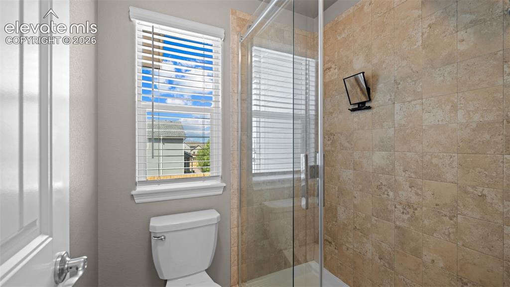 Image 25 of 43: Shower enclosure with clear glass door, stone-finish tile surround, and a w