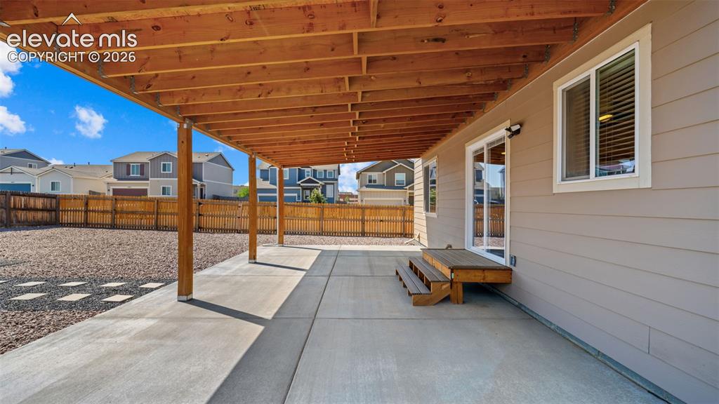Image 33 of 43: Expansive concrete patio with a covered wood-beam deck overhead, offering d