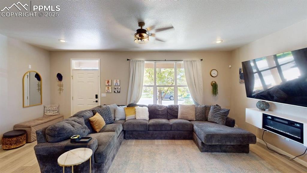 Image 5 of 14: Living room with light wood-type flooring, a ceiling fan, and a textured ce