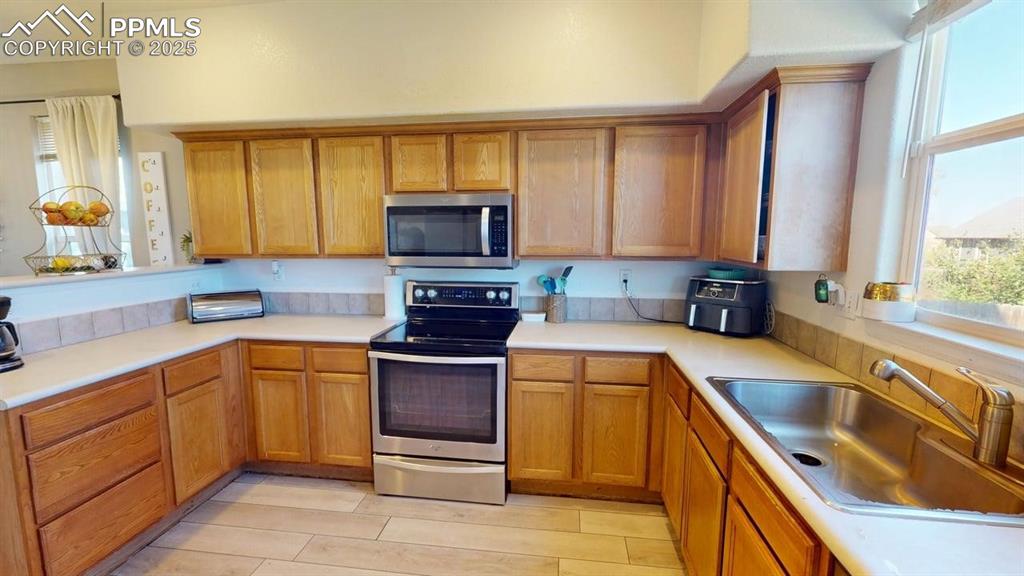 Image 8 of 14: Kitchen featuring stainless steel appliances, brown cabinets, and light cou