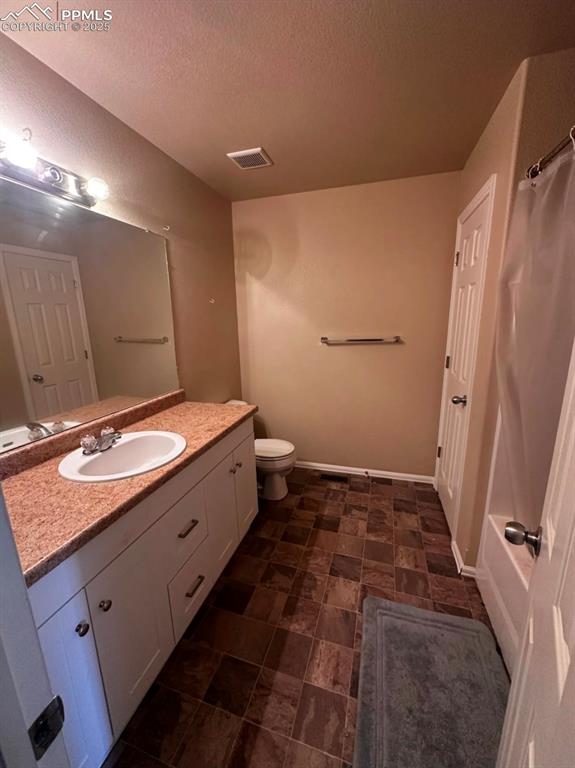Image 20 of 21: Bathroom with vanity, a textured ceiling, curtained shower, and stone finis