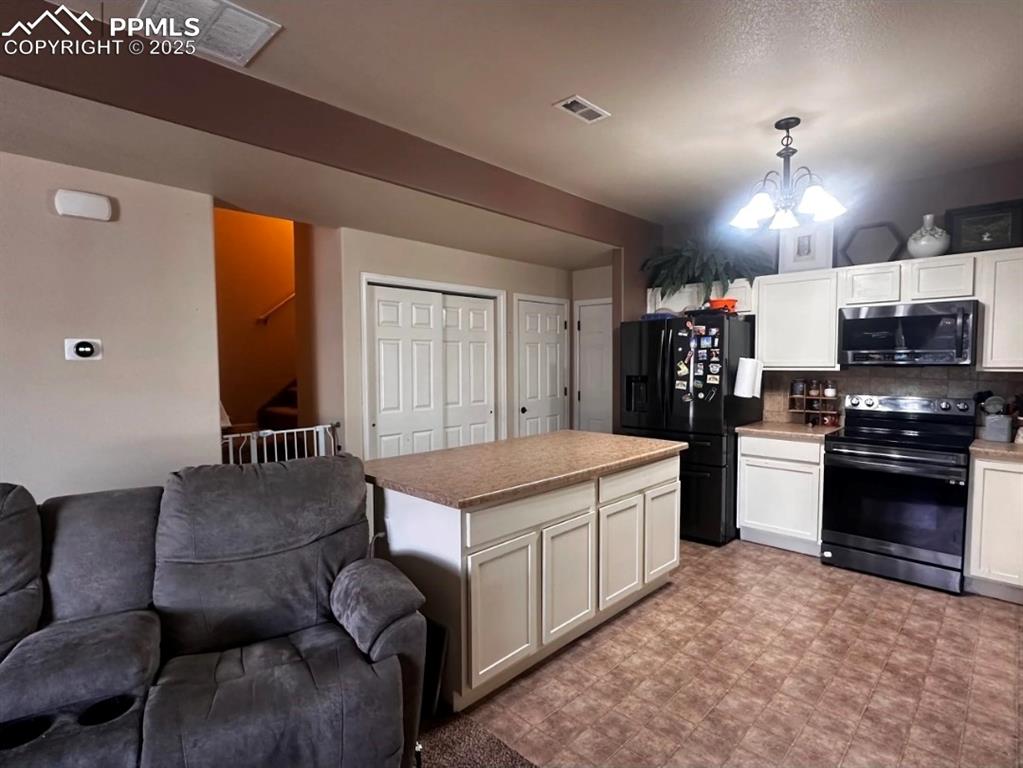 Image 8 of 21: Kitchen with electric range oven, white cabinets, black refrigerator with i