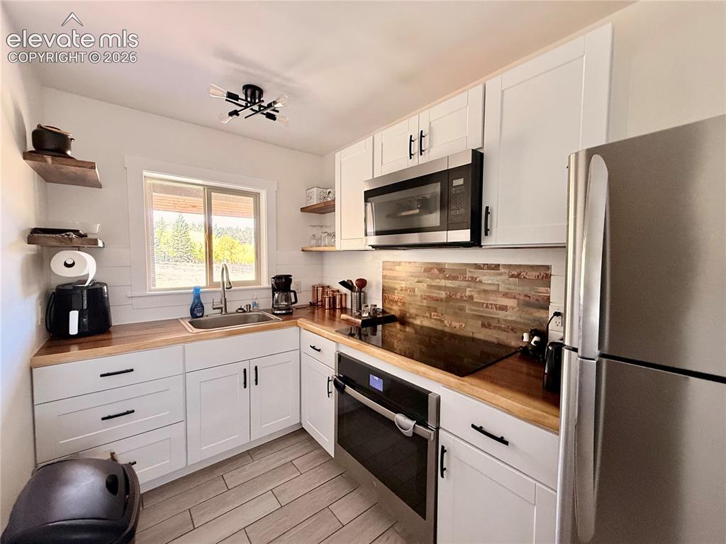 Image 11 of 43: White cabinetry with matte black hardware, wood-finish countertops, stainle