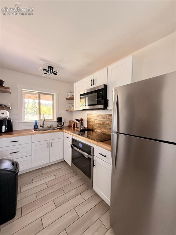 Image 12 of 43: White shaker cabinetry with black hardware, wood-finish countertops, stainl