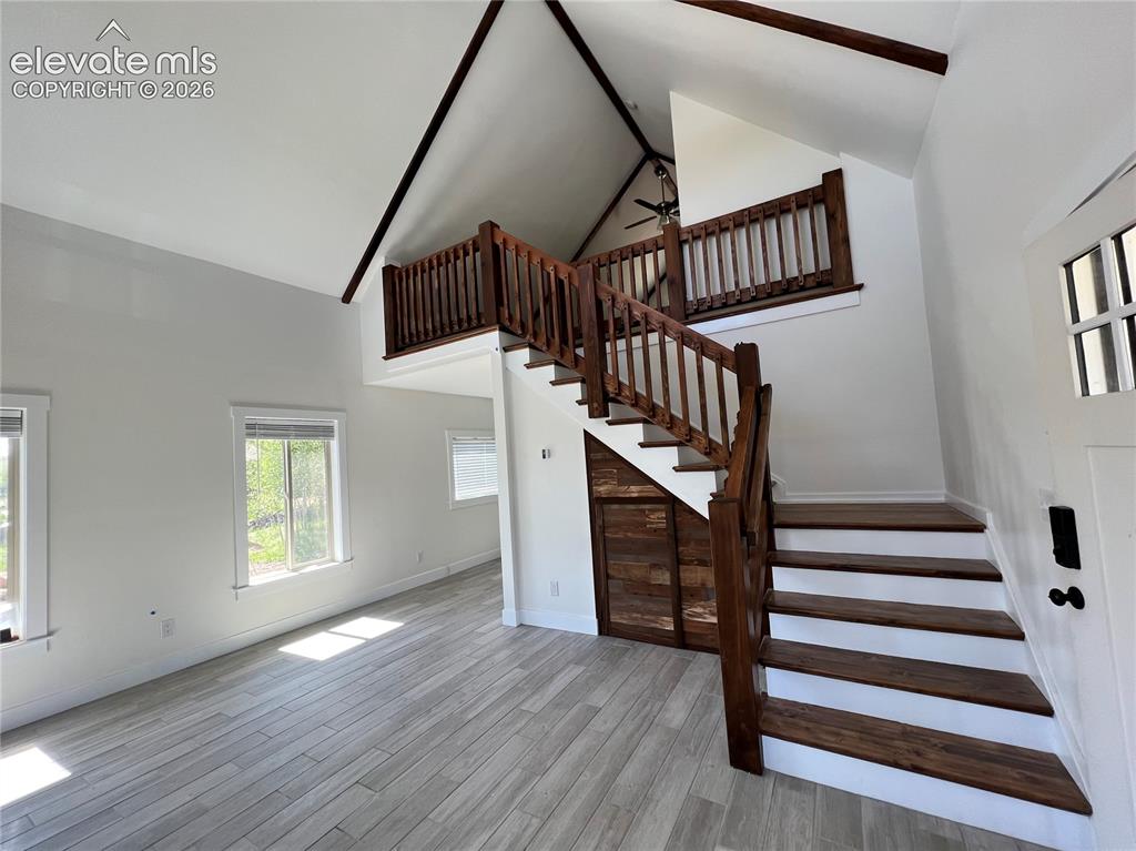 Image 16 of 43: Vaulted ceilings with exposed beams, wood-finish flooring, staircase with w