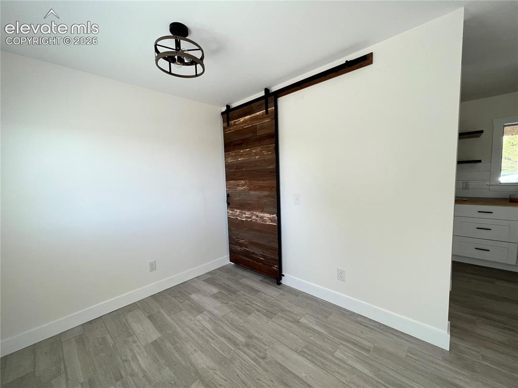 Image 17 of 43: Wood-finish flooring, accent barn door with dark hardware, and a semi-flush