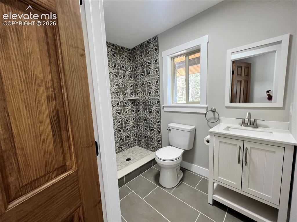 Image 19 of 43: Walk-in shower with decorative tiled surround, single-sink vanity with whit