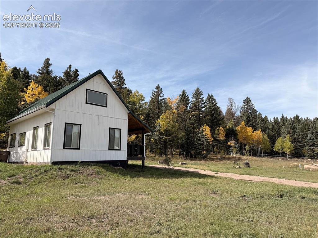 Image 3 of 43: White vertical siding exterior with a dark green gabled roof and black-fram