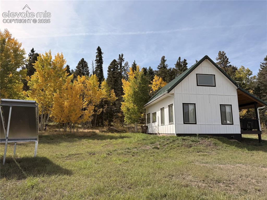 Image 4 of 43: White exterior siding with black trim windows, a dark green gabled roof, an