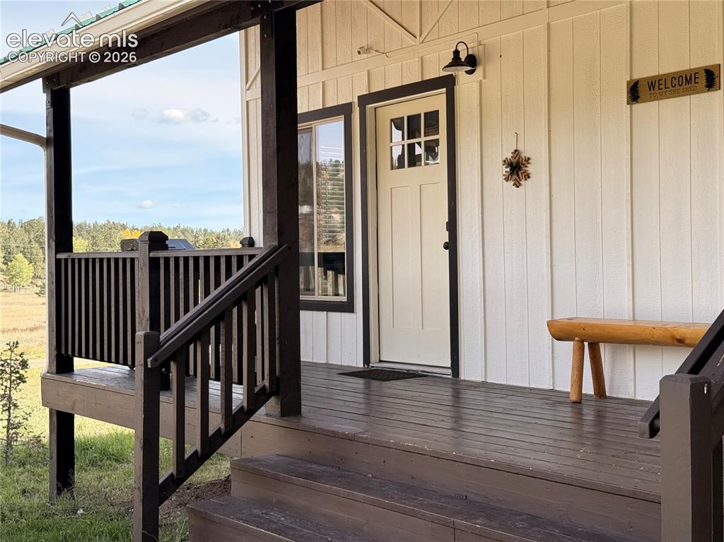 Image 8 of 43: Covered porch with wood flooring, wood railings, and a green roof accent