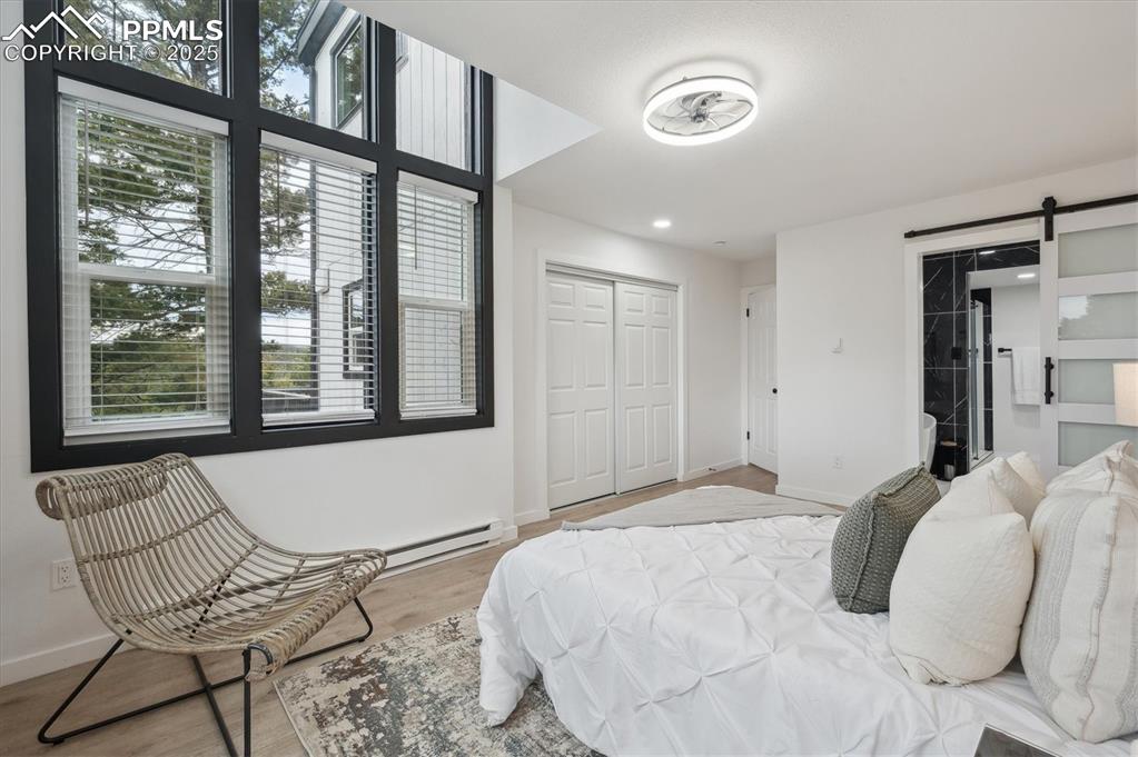 Image 15 of 44: Bedroom with baseboard heating, a barn door, multiple windows, and wood fin