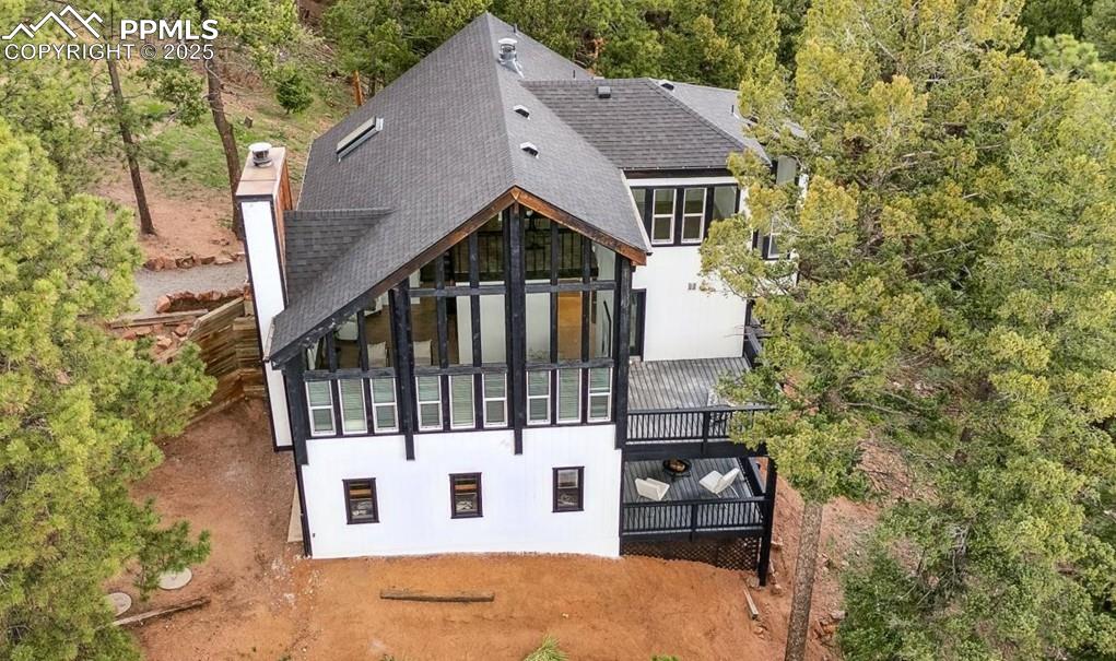 Image 2 of 44: Rear view of house featuring a shingled roof, a chimney, and a wooded view