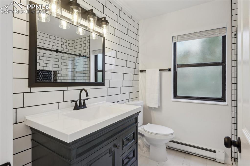 Image 20 of 44: Full bathroom featuring a baseboard radiator, tile walls, vanity, toilet, a