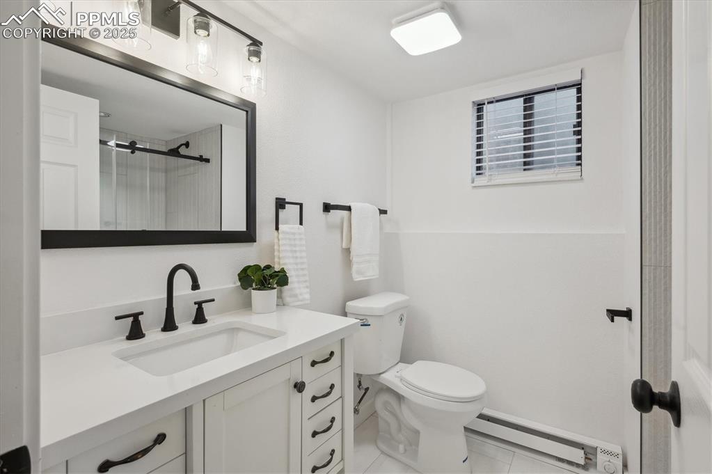 Image 23 of 44: Bathroom featuring a baseboard radiator, vanity, toilet, a shower, and tile