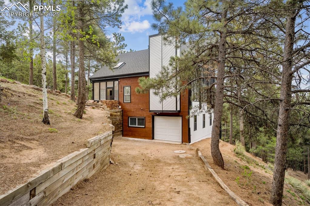 Image 35 of 44: View of side of home with driveway, an attached garage, roof with shingles,