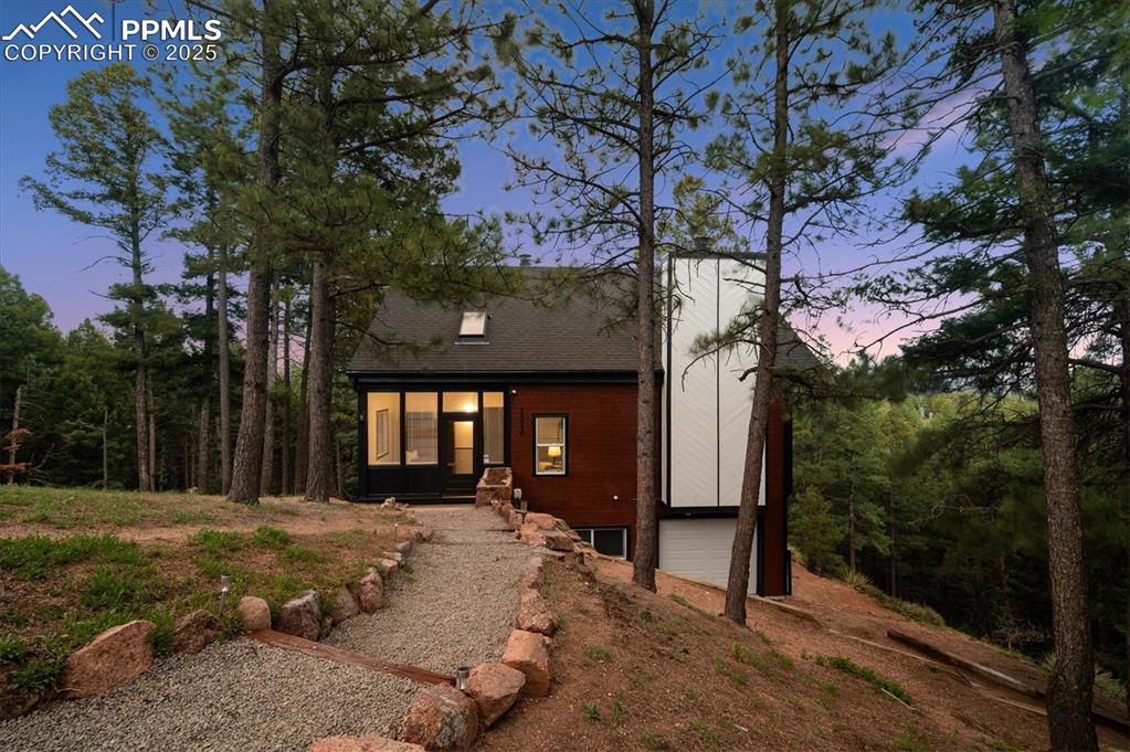 Image 36 of 44: View of front of house featuring a garage, dirt driveway, and roof with shi