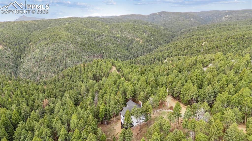 Image 40 of 44: Drone / aerial view of a heavily wooded area and a mountainous background