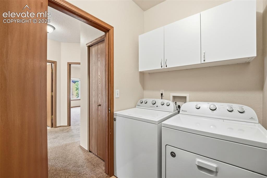 Image 13 of 30: Dedicated laundry area featuring white upper cabinetry, a top-load washing 