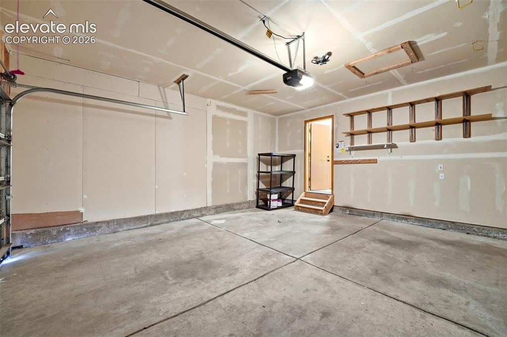 Image 14 of 30: Spacious garage featuring a concrete floor, built-in wooden shelving, an ov