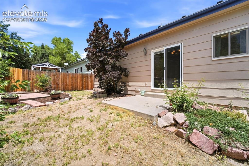 Image 21 of 30: Rear exterior featuring tan horizontal siding and a sliding glass door