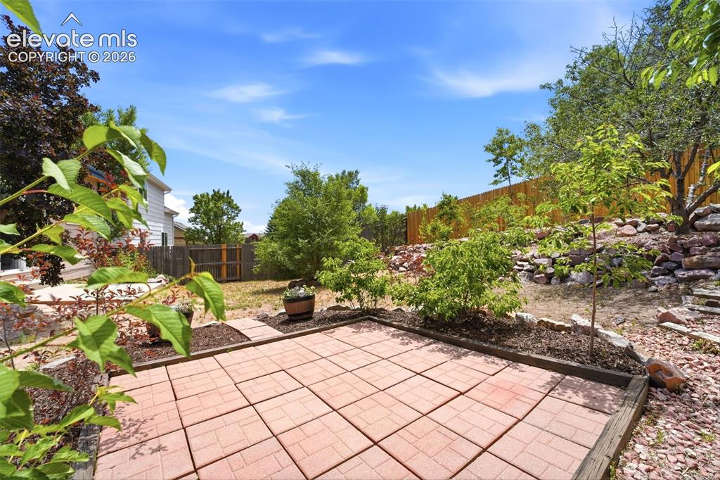 Image 22 of 30: Brick paver patio with a wood border, surrounded by landscaped garden beds,