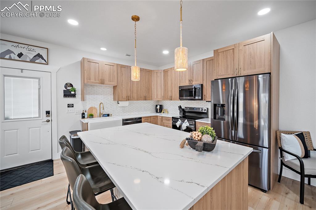 Image 23 of 47: Kitchen with light brown cabinetry, stainless steel appliances, decorative