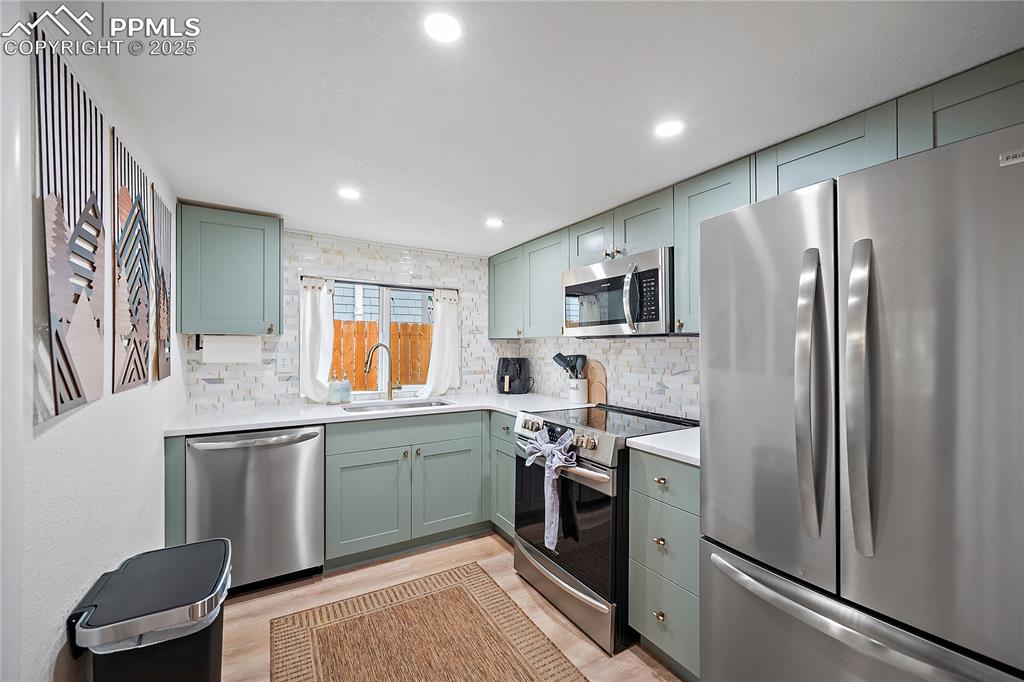 Image 9 of 47: Kitchen with a sink, green cabinets, stainless steel appliances, and backsp