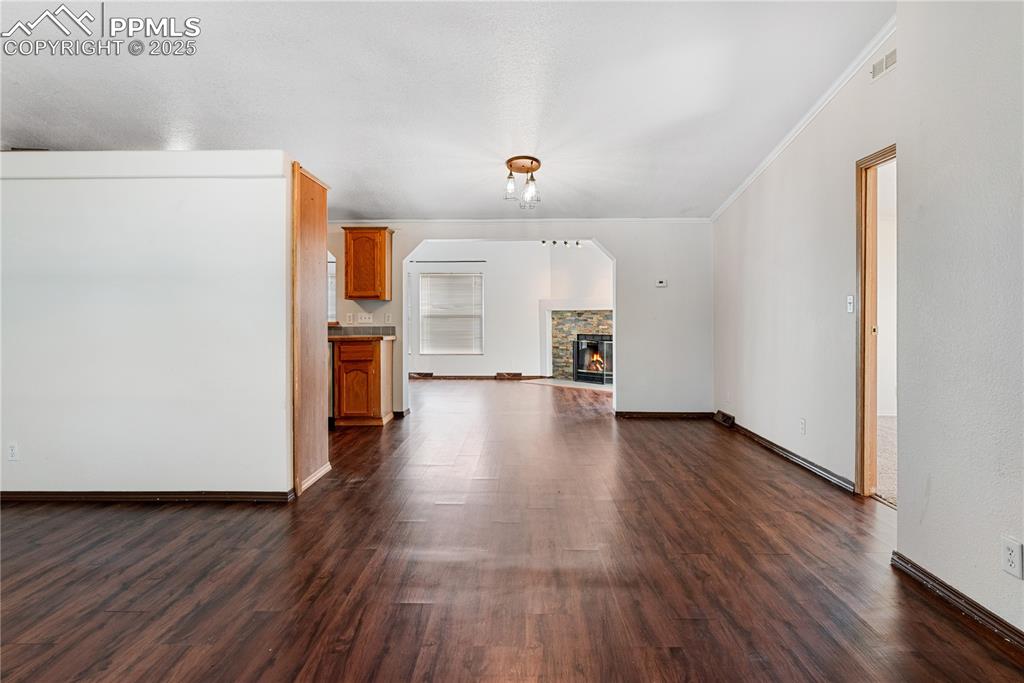Image 13 of 46: Unfurnished living room featuring ornamental molding, dark wood-style floor