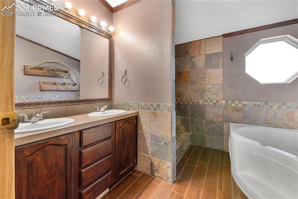 Image 18 of 46: Full bath with crown molding, a garden tub, tile walls, double vanity, and