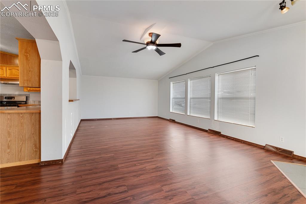 Image 24 of 46: Unfurnished living room featuring ceiling fan, vaulted ceiling, and dark wo