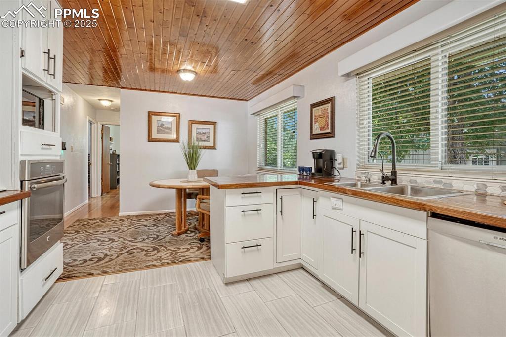 Image 10 of 38: Kitchen with white cabinetry, wooden ceiling, butcher block counters, dishw