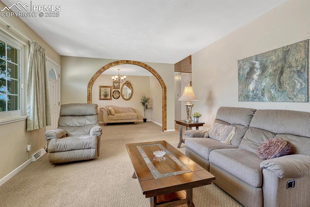 Image 6 of 38: Carpeted living area with arched walkways and a chandelier