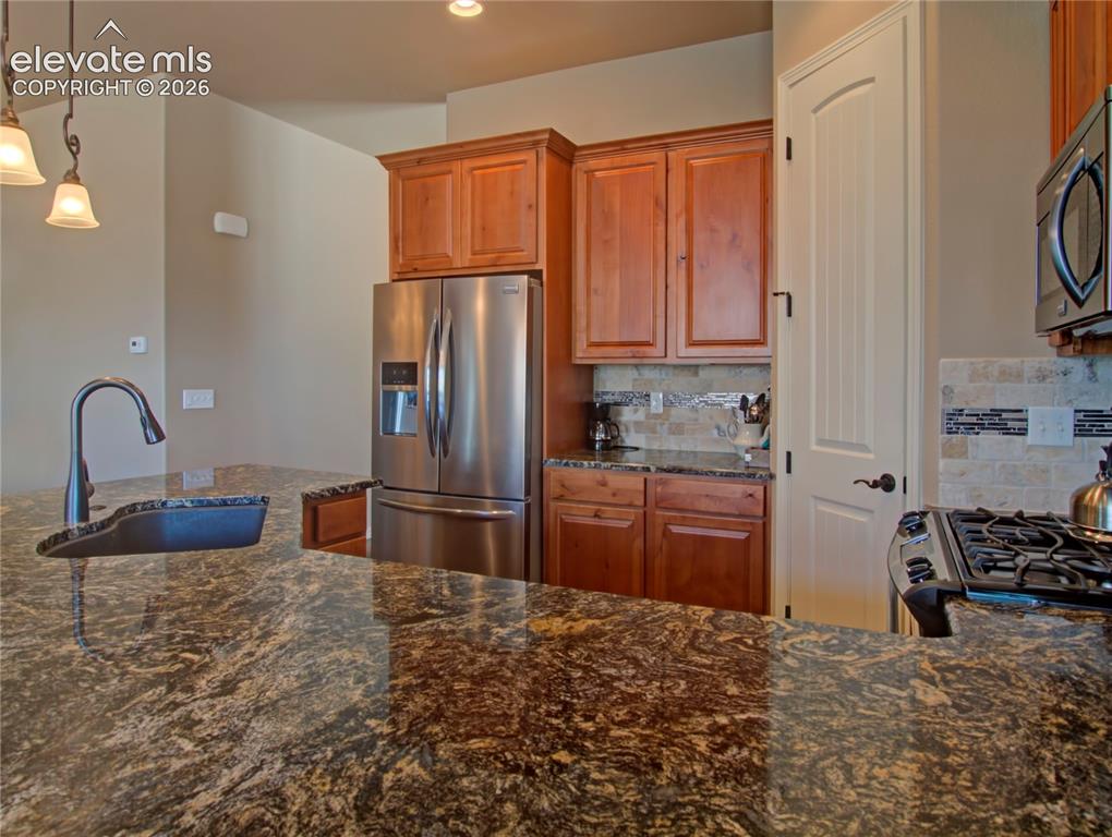 Image 10 of 33: Spacious kitchen featuring expansive stone countertops, wood cabinetry, sta