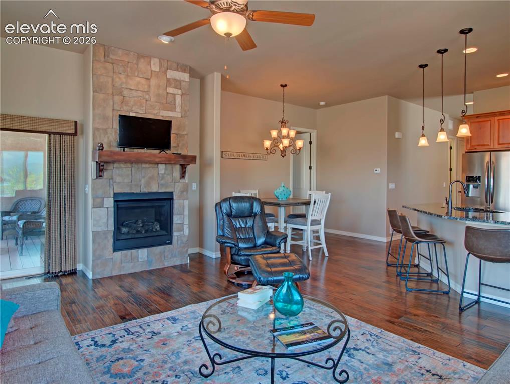 Image 12 of 33: Open-concept living area with wood-finish flooring, a stone-faced fireplace