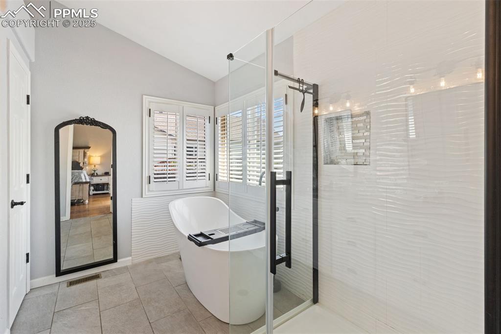 Image 29 of 39: Full bathroom with vaulted ceiling, a freestanding tub, a stall shower, and