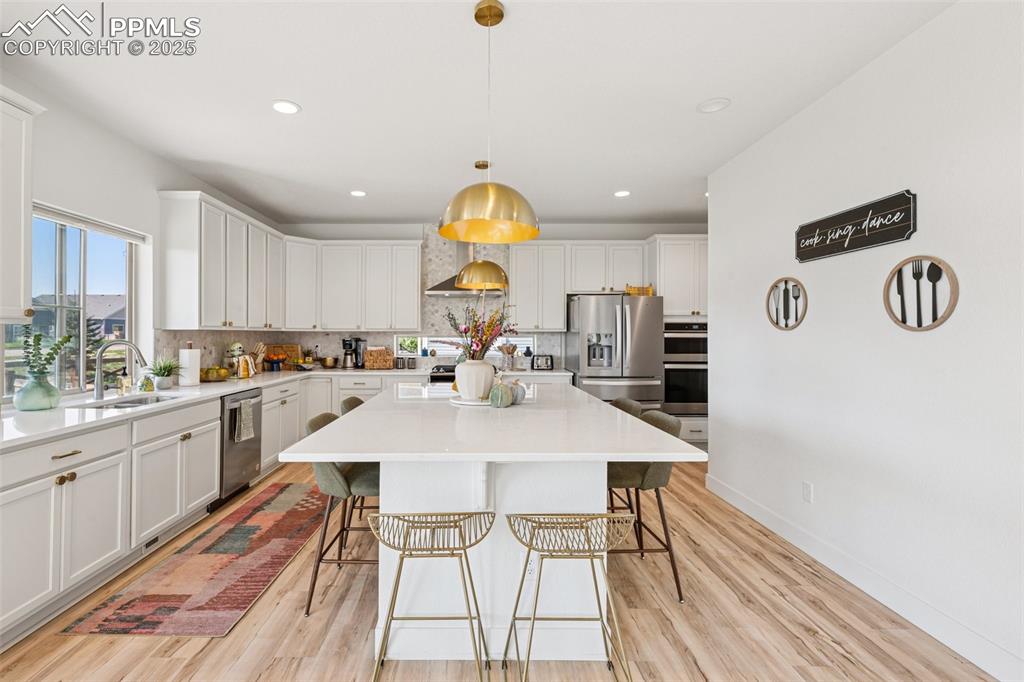 Image 14 of 43: Kitchen featuring backsplash, white cabinetry, a breakfast bar, light wood 