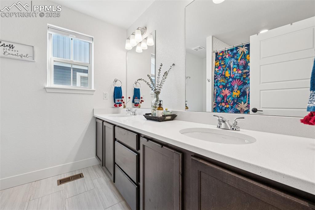 Image 32 of 43: Bathroom featuring double vanity, a shower with curtain, and light tile pat