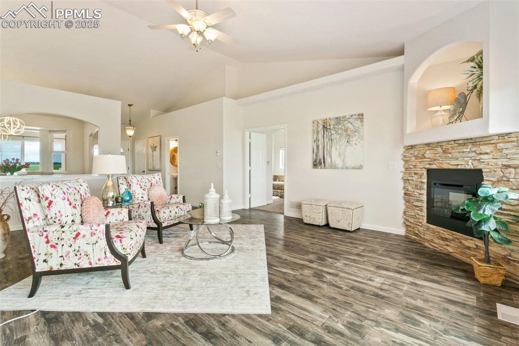 Image 16 of 44: Living area with wood finished floors, ceiling fan, a stone fireplace, and