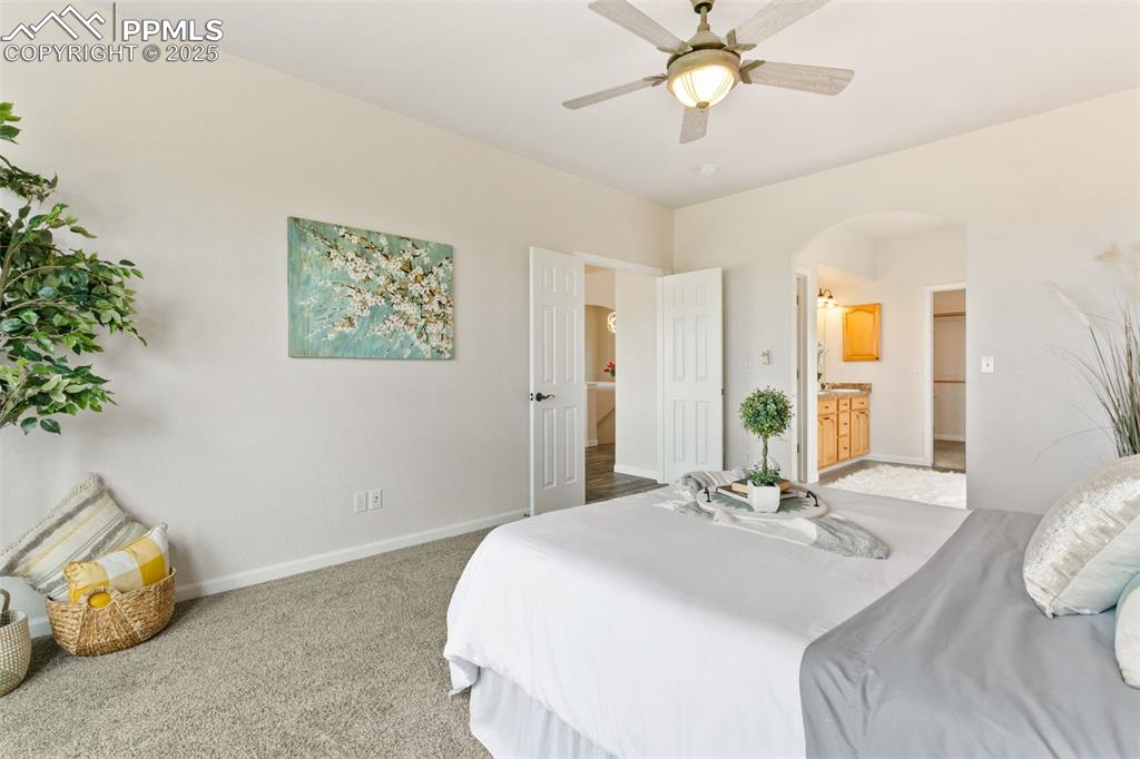 Image 25 of 44: Carpeted bedroom featuring arched walkways, ensuite bath, and a ceiling fan