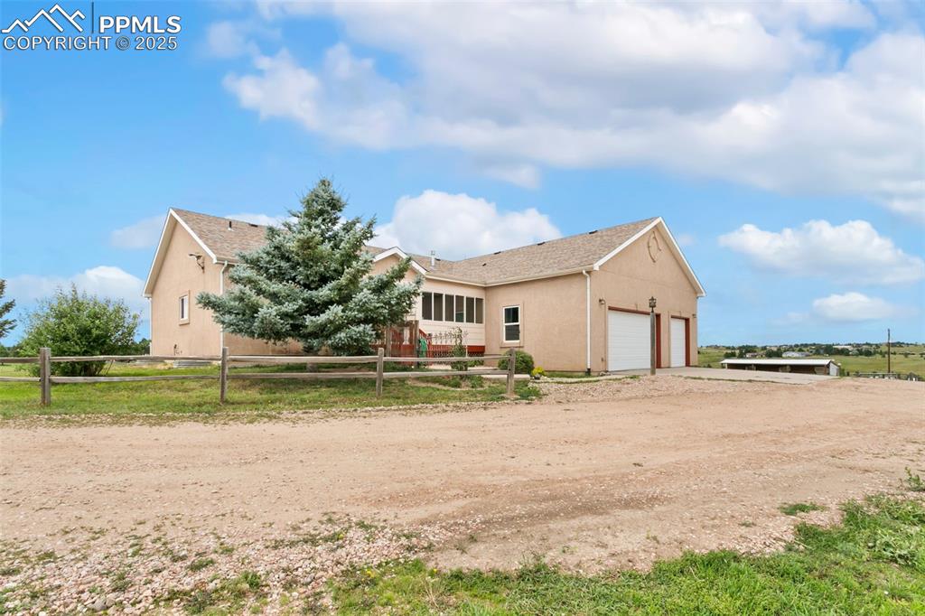 Image 40 of 44: View of side of property featuring dirt driveway, stucco siding, and a gara
