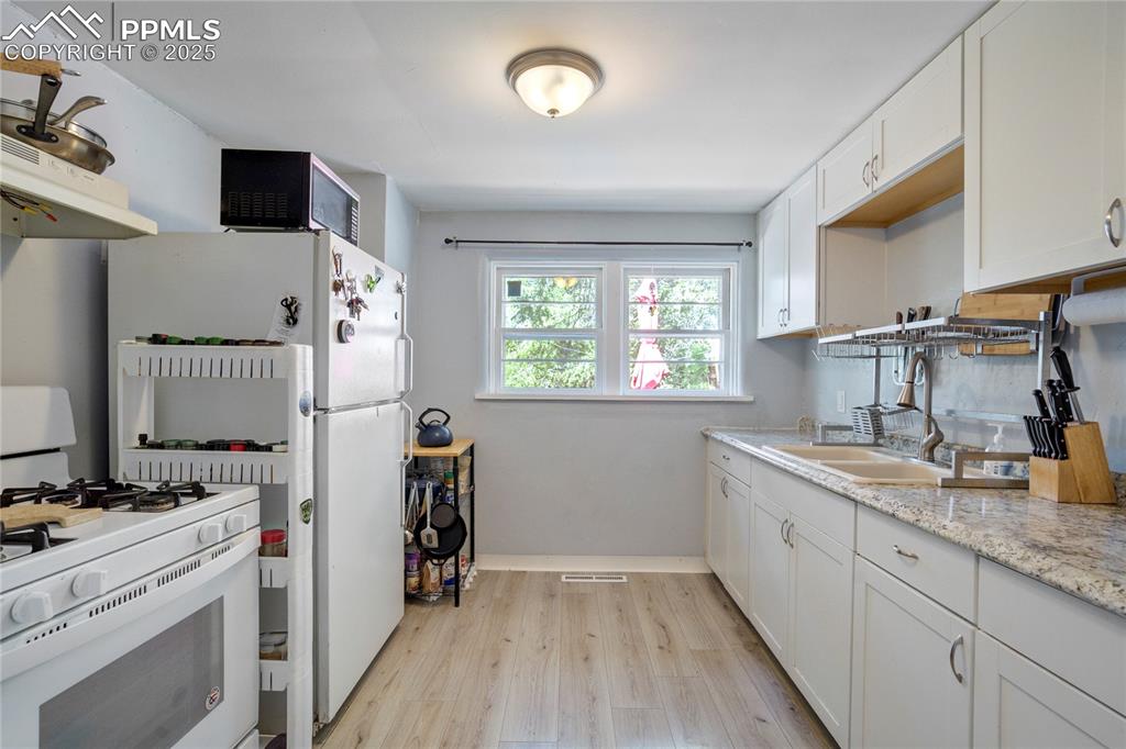 Image 10 of 28: Kitchen with white appliances, light wood-style flooring, white cabinetry, 