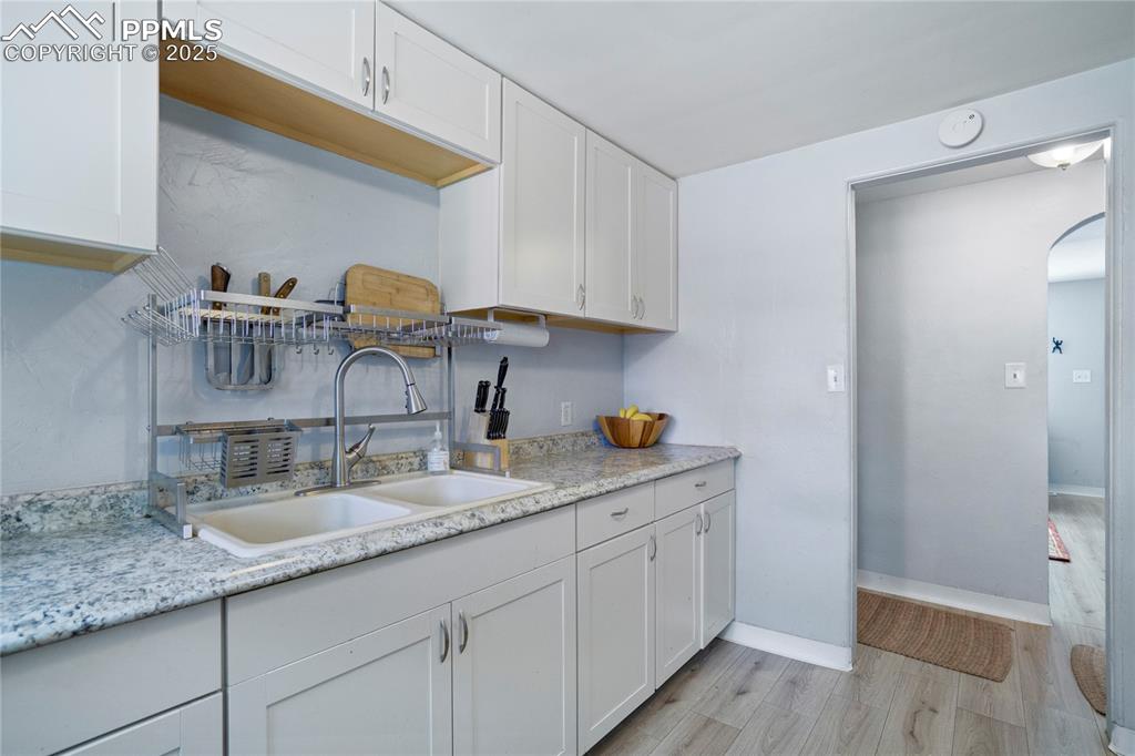 Image 11 of 28: Kitchen featuring white cabinets, light wood finished floors, and arched wa
