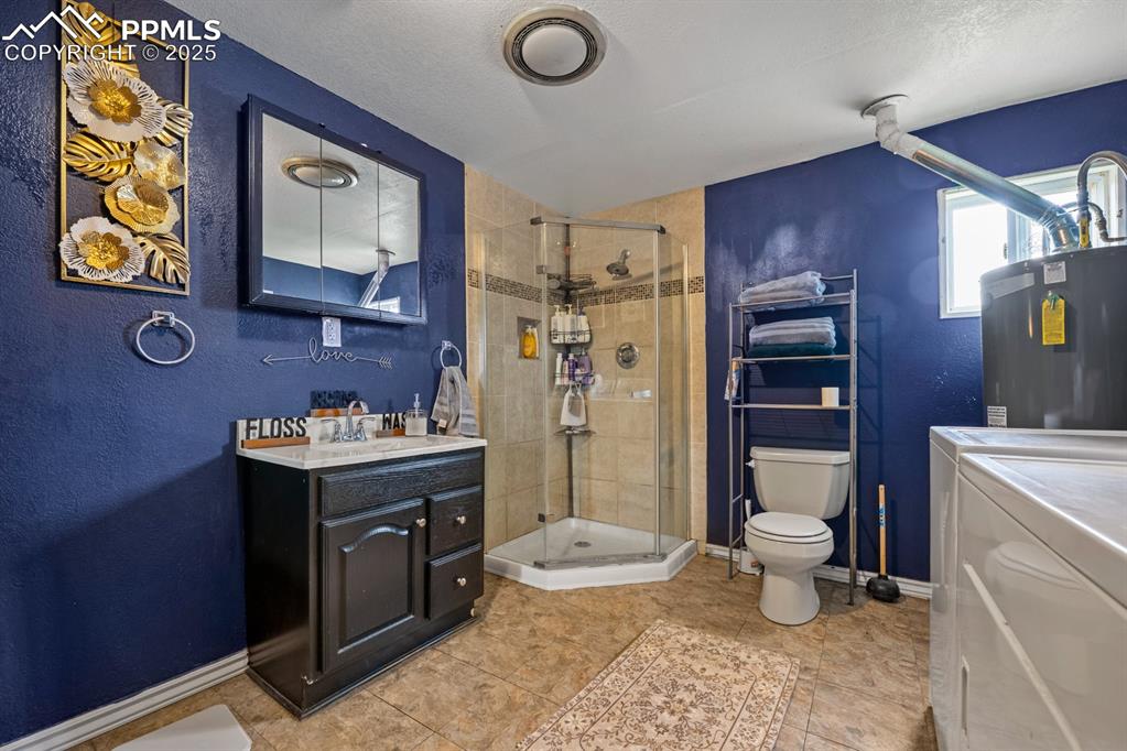 Image 14 of 24: Bathroom with a textured wall, vanity, a stall shower, water heater, and a