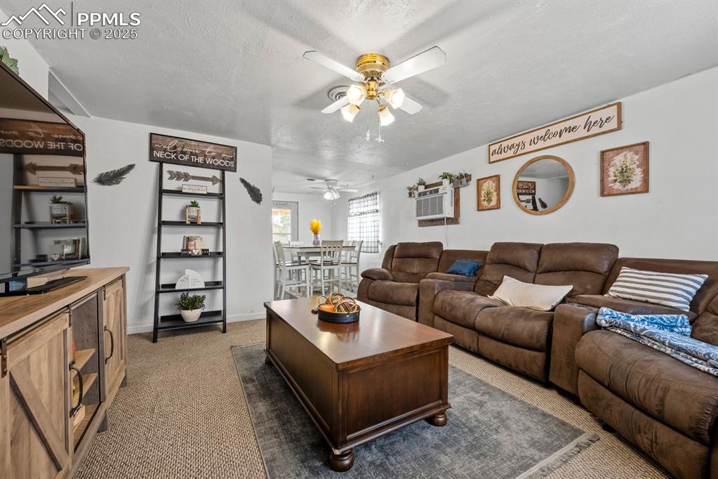 Image 4 of 24: Living area with carpet flooring, a textured ceiling, ceiling fan, and a wa
