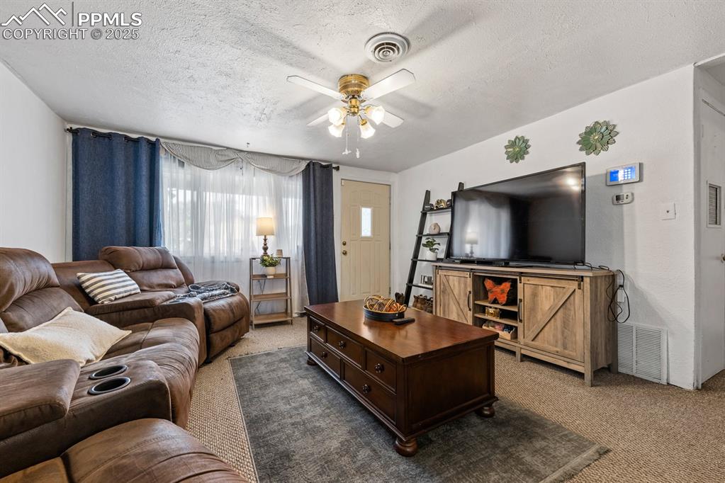 Image 5 of 24: Carpeted living room featuring a textured ceiling and ceiling fan
