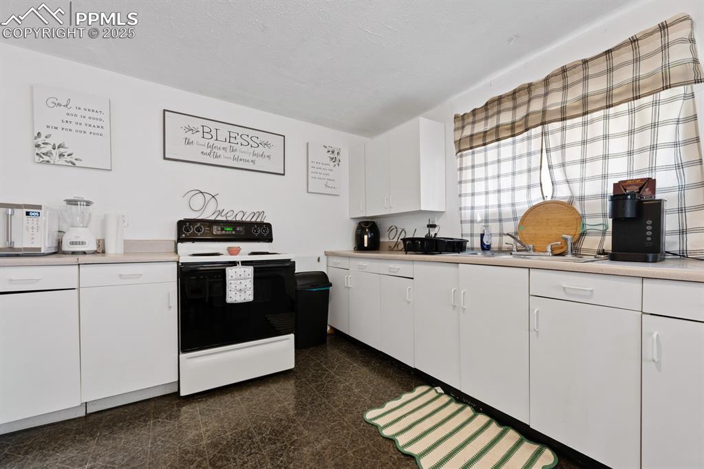 Image 7 of 24: Kitchen with white cabinetry, electric stove, light countertops, and white
