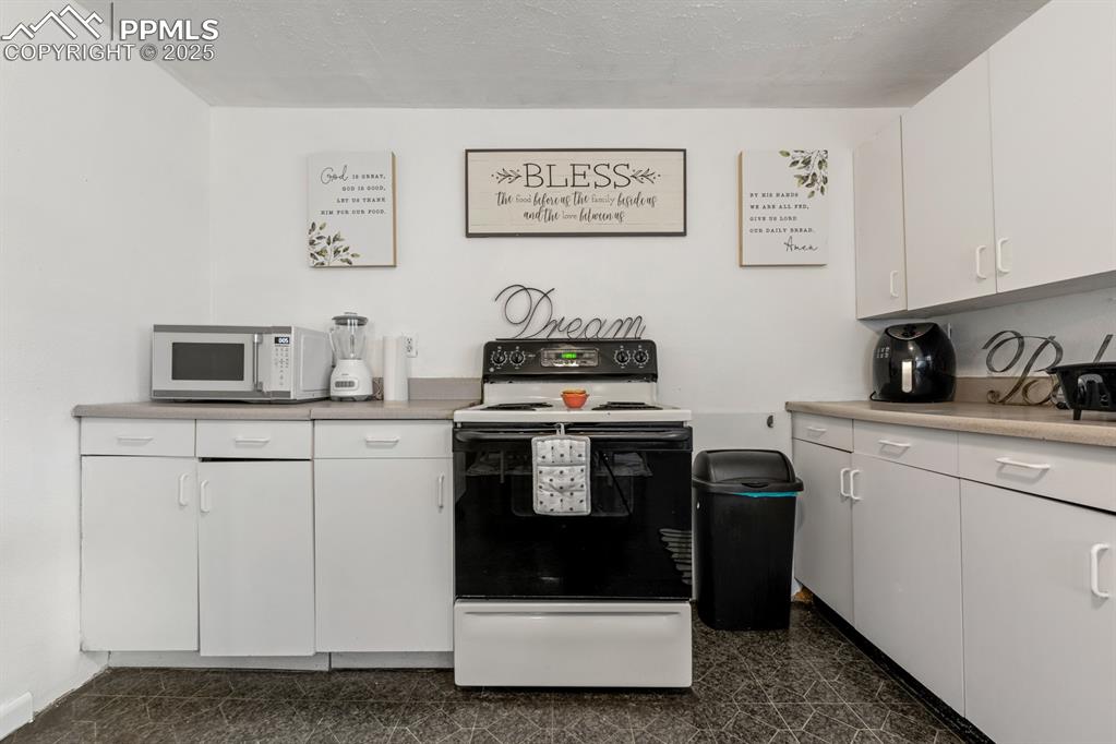 Image 8 of 24: Kitchen with range with electric stovetop, white cabinets, white microwave,